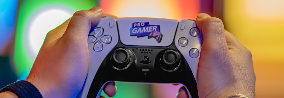 Two hands are holding a gaming controller labeled 'Pro Gamer'. The background is blurred with colorful lights creating a vibrant atmosphere.